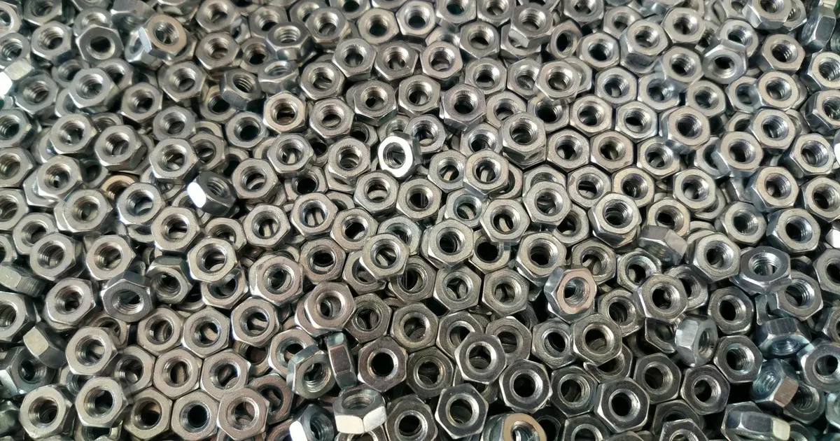 Pile of small hex nuts in a metal surface texture, photographed from above